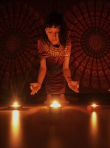 A woman in a spiritual ritual setting surrounded by lit candles indoors.