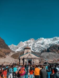 A large gathering of tourists at the Kedarnath Temple in the Himalayas, under a clear blue sky.