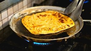 Golden brown paratha being cooked on a skillet, showcasing traditional flatbread preparation.