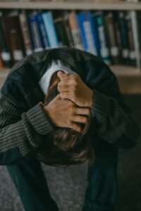 Person sitting with head down and hands on head in a library setting.