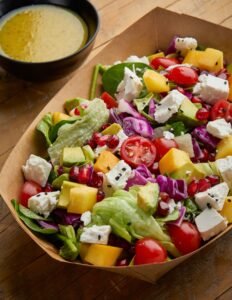 Colorful mixed salad with fresh vegetables, cheese, and dressing in a paper bowl, ideal for healthy eating.