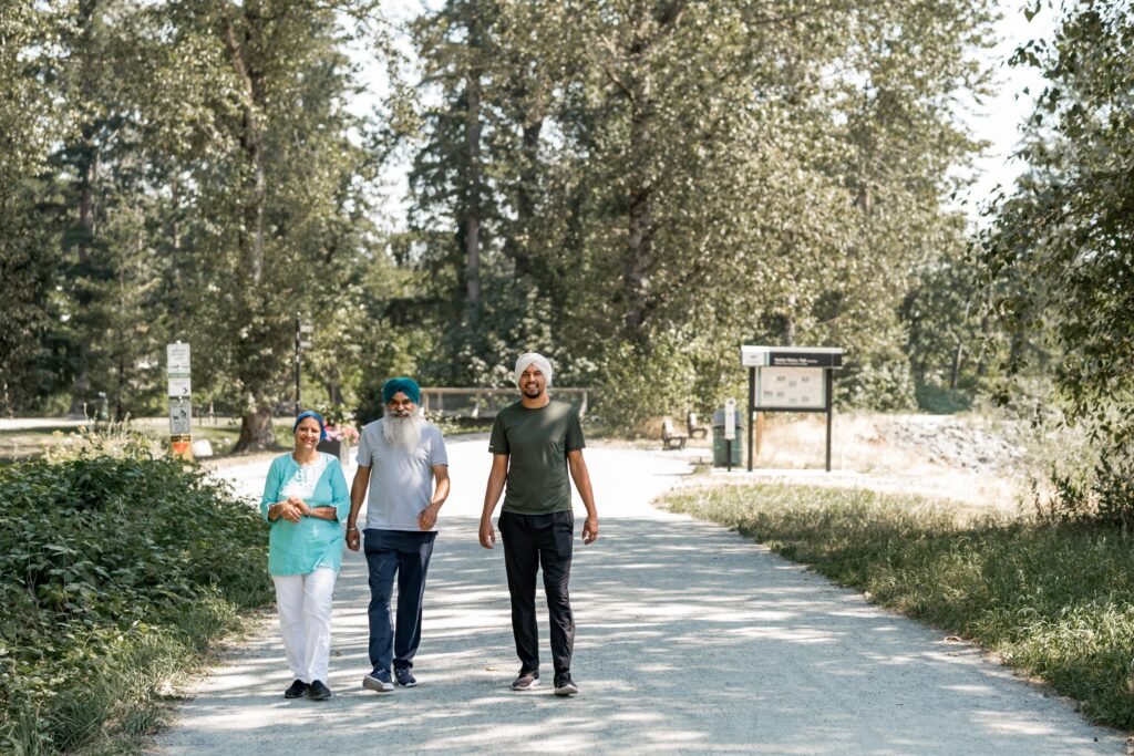 A family strolls down a sun-dappled park path on a clear day.