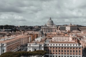 Skyline view of Vatican City featuring St. Peter's Basilica under a cloudy sky.
