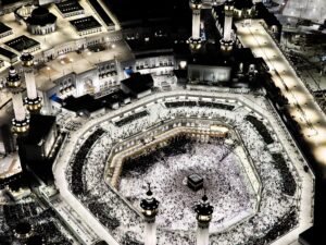 Stunning aerial photograph of the Grand Mosque in Mecca, illuminated at night, showcasing the Kaaba and worshippers.