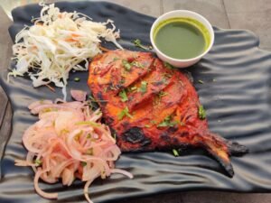 Deliciously grilled pomfret served with onions, coleslaw, and green sauce on a black plate.