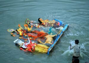 Vibrant Hindu deity idols are immersed in a river during a traditional ceremony.
